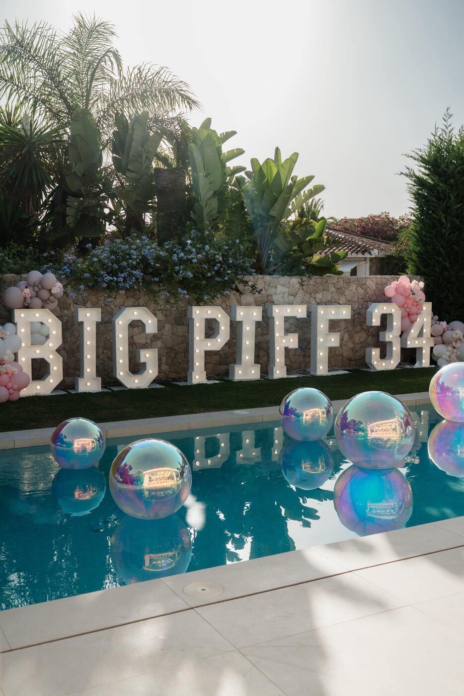 Light-up BIG PIFF 34 letters with pink balloon clusters and iridescent orbz floating in a pool, Marbella villa